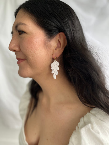 White and gold leaf dangle earrings on models ear