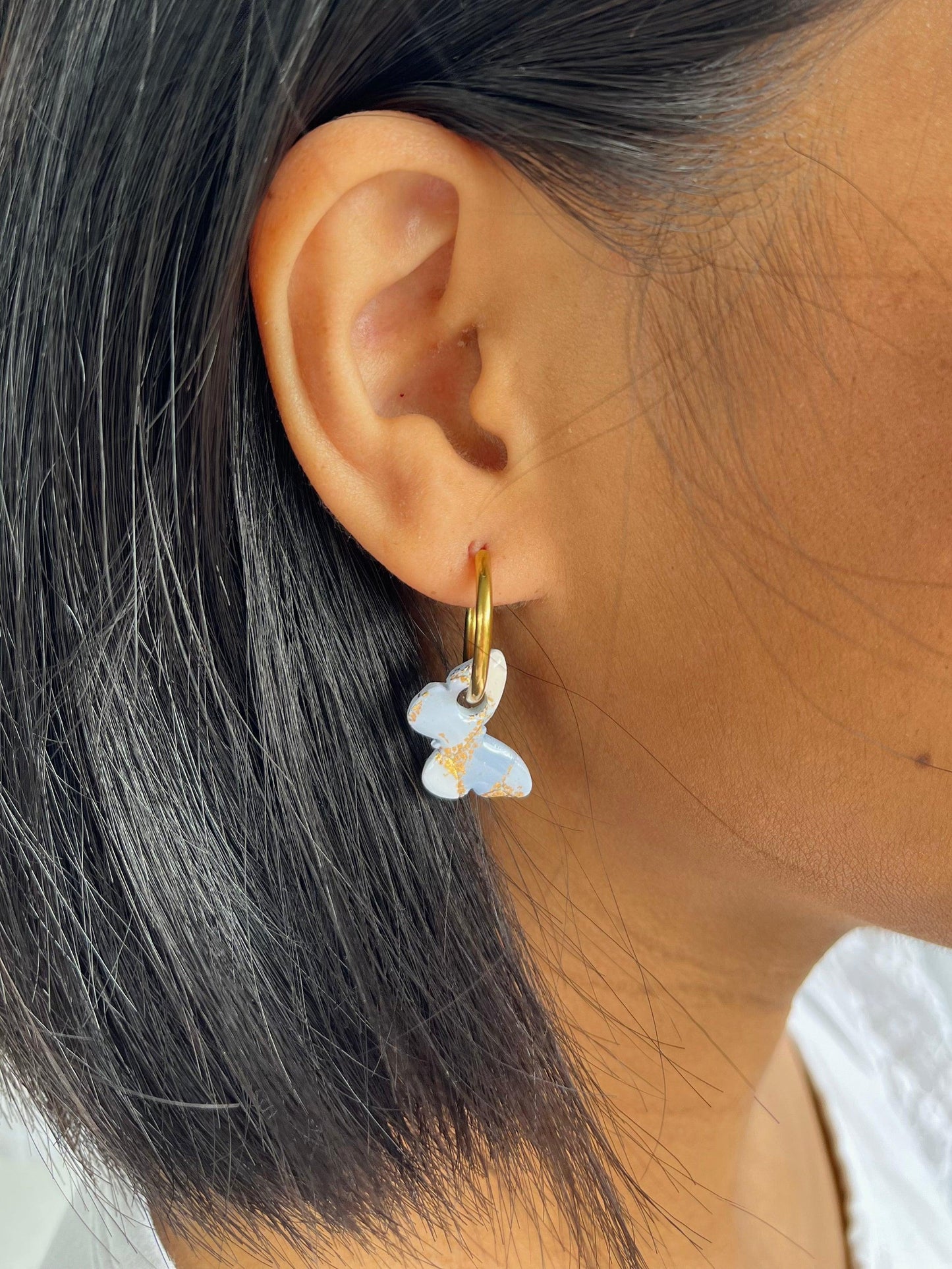 Close up of blue and gold small butterfly hoop earrings on models ear