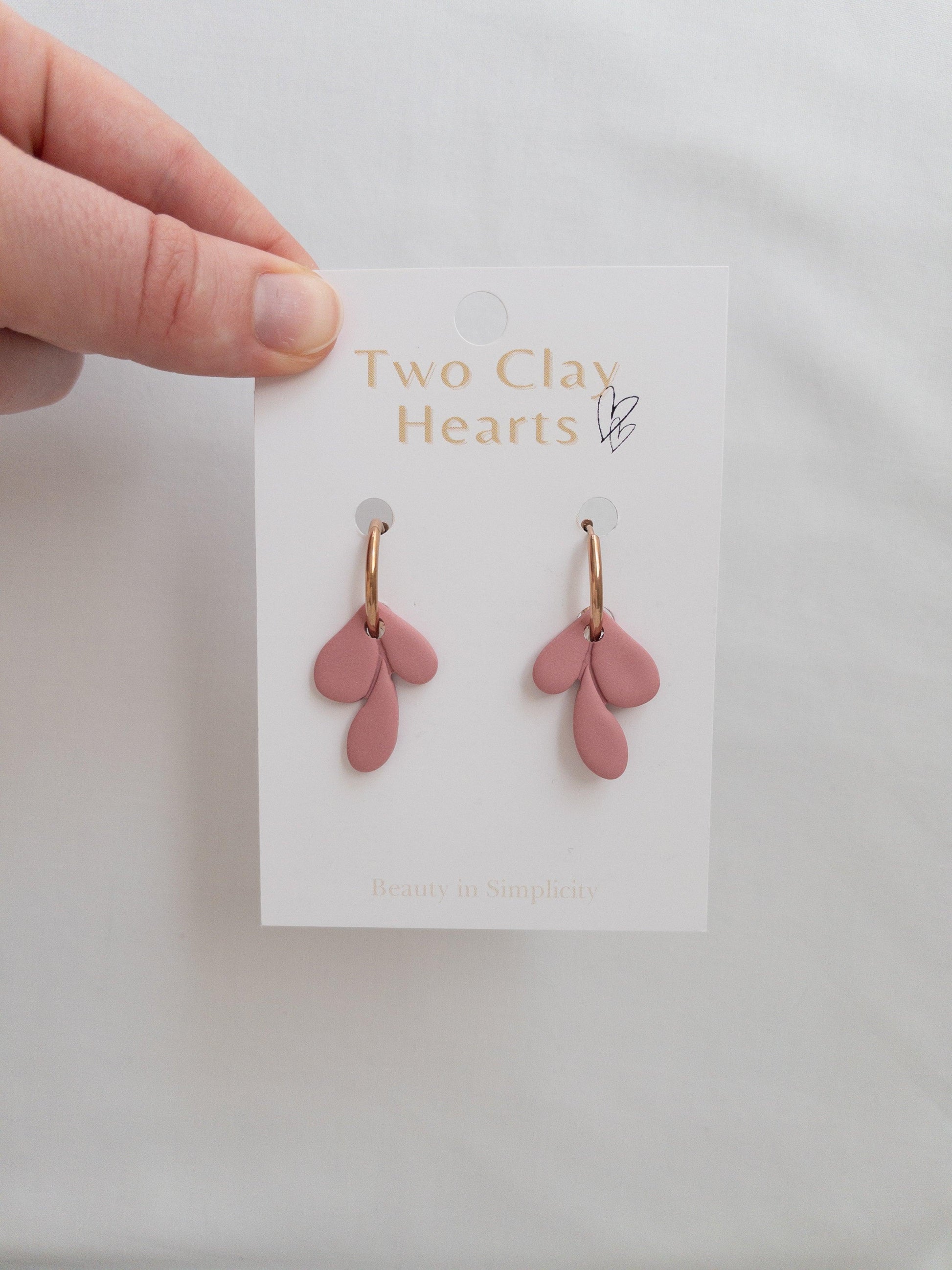 Elegant rose gold and maroon leaf hoop earrings on white backing card