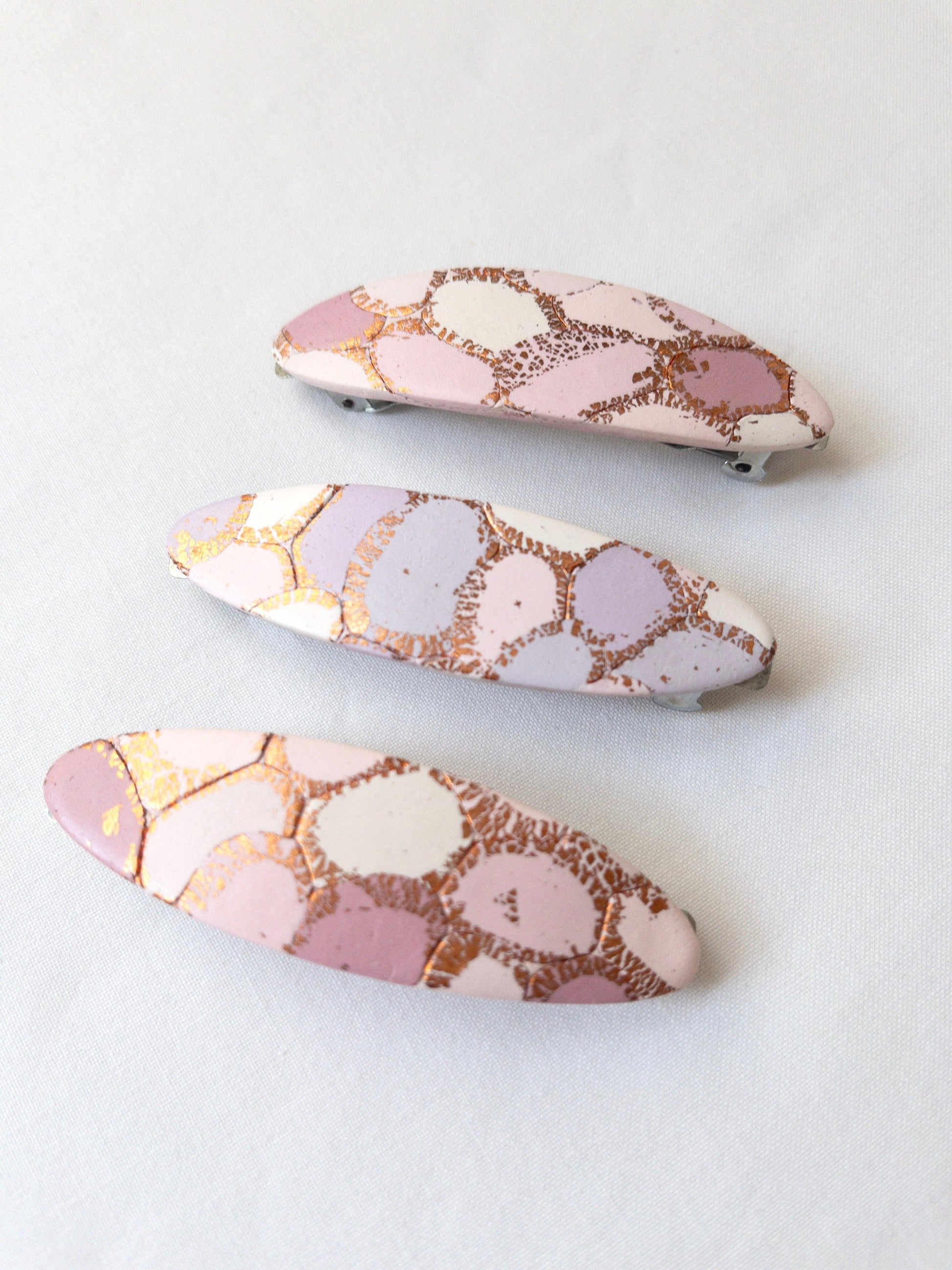 Polymer Clay oval hair clips with pastel and gold patterns on a white background