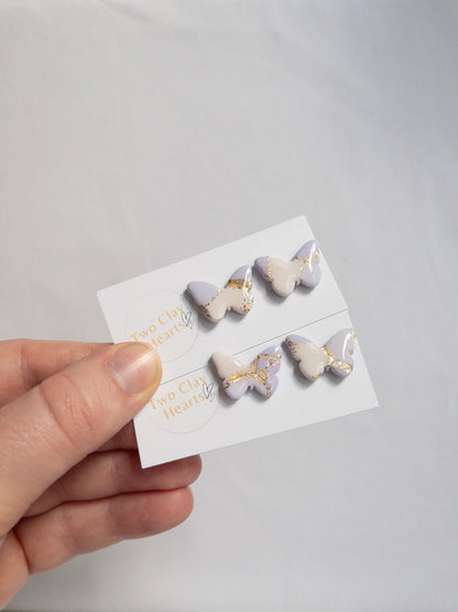 two pairs of purple and white butterfly stud earrings with shiny gold flecks