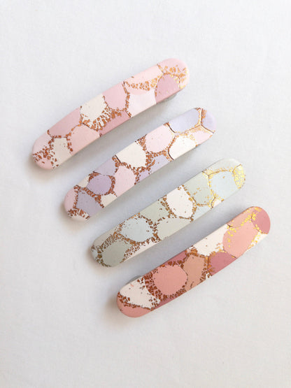 Pastel and gold patterned polymer clay hair clips on white background