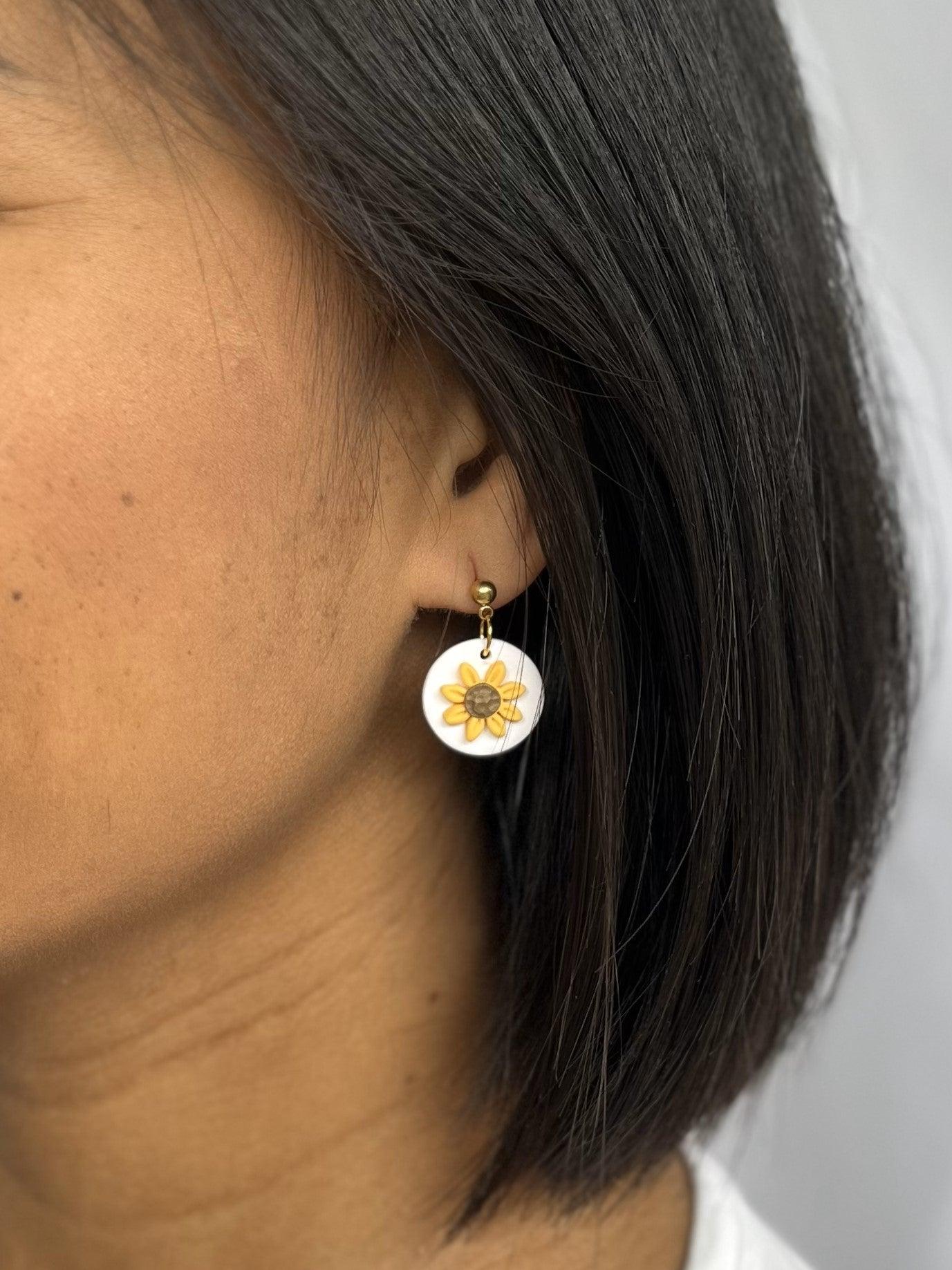 Close up of small sunflower dangle earrings with gold ball top on models ear